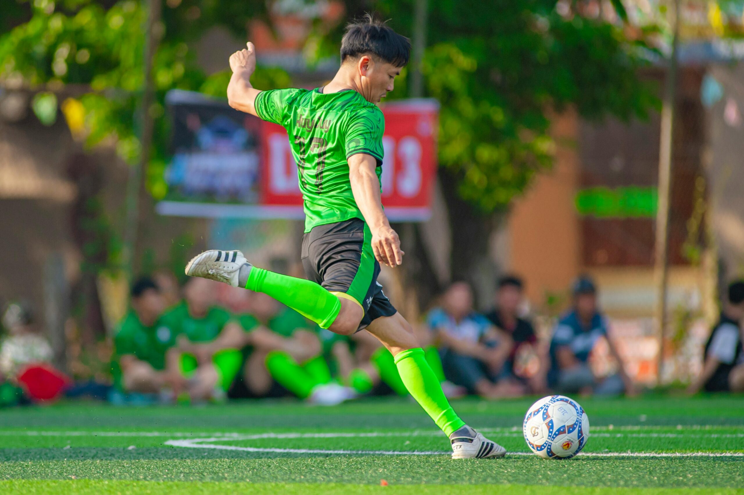 Ein Fußballspieler in grüner Uniform kickt den Ball während eines Sportspiels in Hà Ná»™i gekonnt.