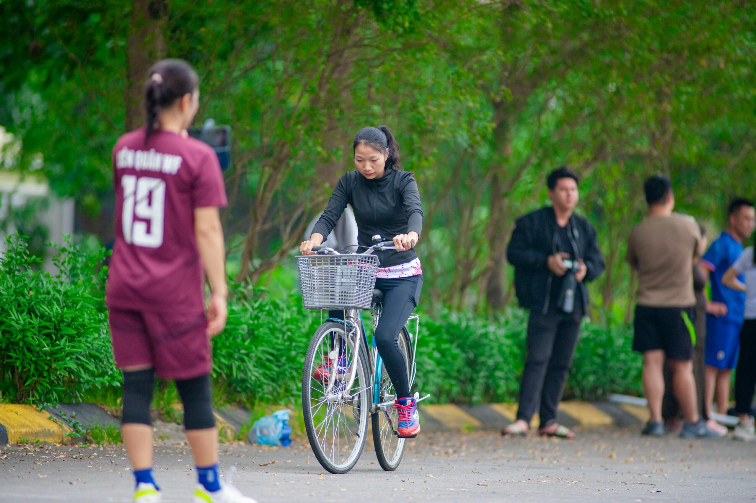 Eine Frau fährt in einem Park in Hanoi Fahrrad, während andere zuschauen oder spielen. Lebendiger Outdoor-Lebensstil.